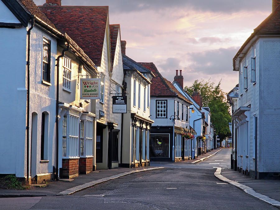 Quaint town street lined with white shopfronts and red-tiled roofs under a soft evening sky, empty and calm.